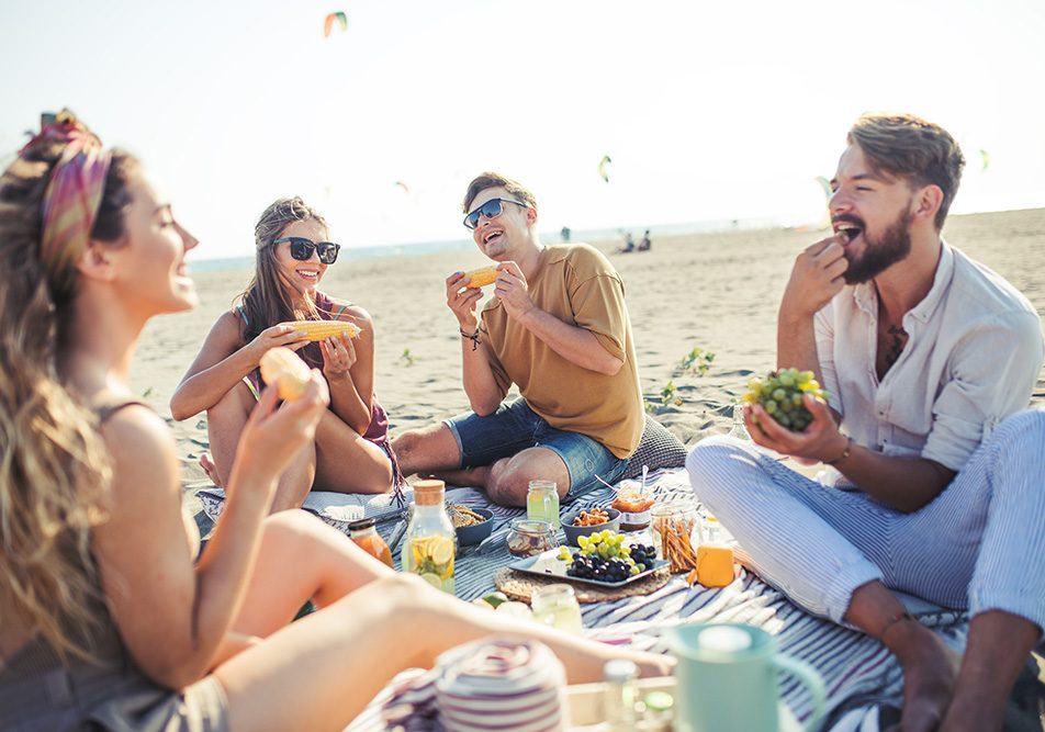 Amici durante un picnic sulla spiaggia, che consumano alimenti freschi e leggeri per evitare i sintomi della gastrite