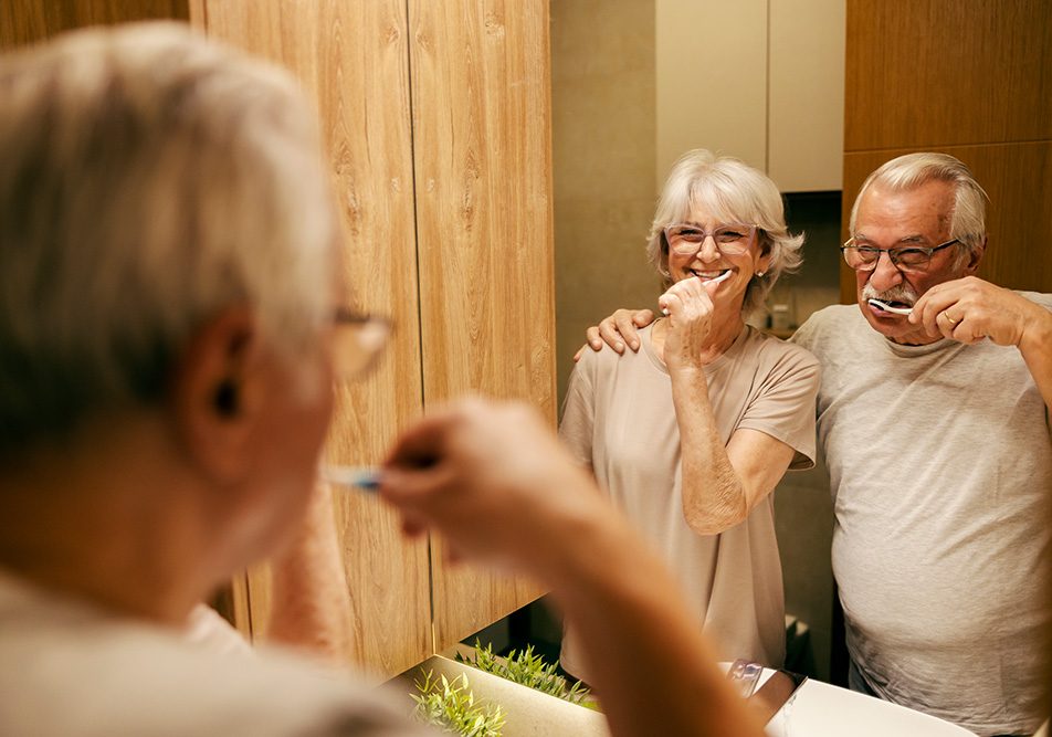 Coppia anziana in bagno davanti allo specchio che segue le indicazioni del dentista su quante volte lavare i denti