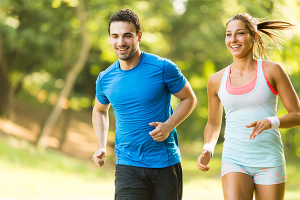 Giovane coppia che combatte i sintomi della digestione lenta praticando jogging al parco tutte le mattine