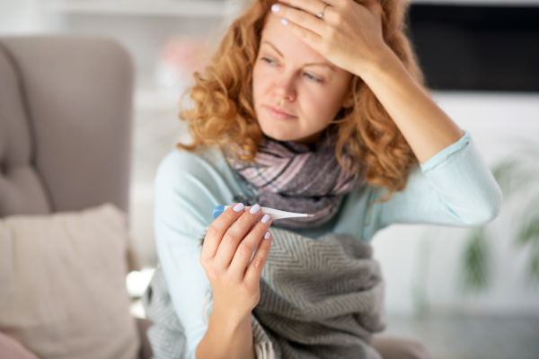 Donna con i sintomi dell'influenza mentre si misura la febbre