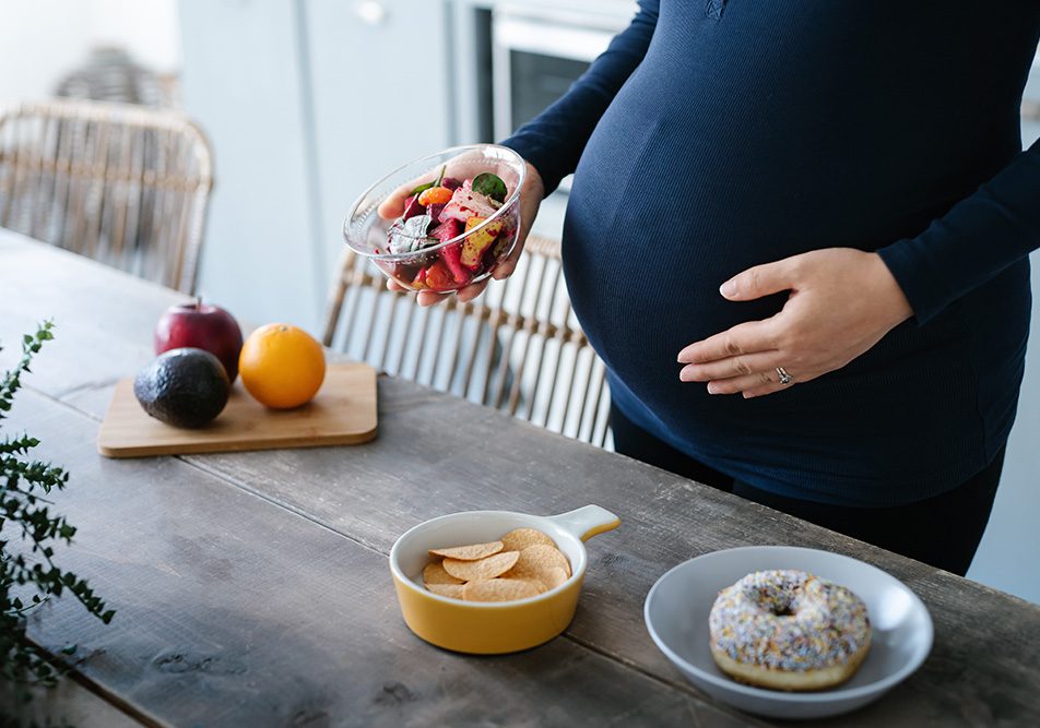Donna con celiachia e disturbi ginecologici che ha voglie di cibo durante la gravidanza e seleziona dal tavolo una macedonia di frutta