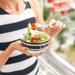 Donna che mangia insalate estive mentre è affacciata al balcone