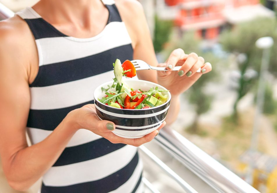 Donna che mangia insalate estive mentre è affacciata al balcone