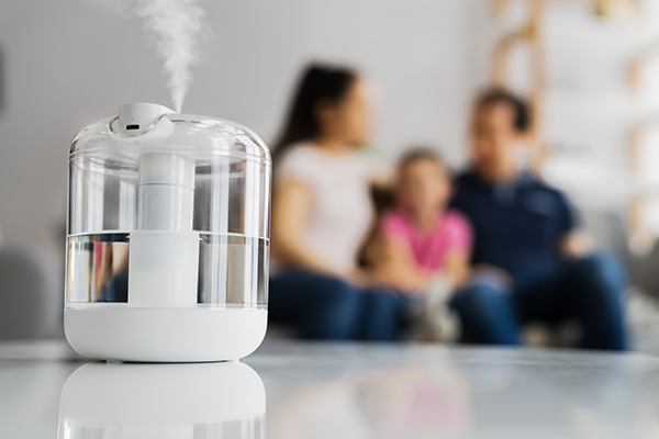 Famiglia sul divano composta da madre, padre e figlia, che attiva l’umidificatore ambiente per favorire una corretta respirazione all'interno degli ambienti domestici
