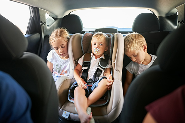 Tre figli che si addormentano in auto, sui sedili posteriori, durante un viaggio; il bambino più piccolo si rilassa con un ciuccio in bocca