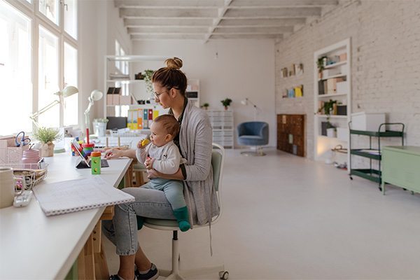 Madre che lavora davanti al laptop con il suo bebè sul grembo durante il periodo di astensione facoltativa di maternità
