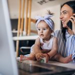 Mamma e bambina che lavorano assieme alla scrivania lavanti al PC; il genitore è al telefono per domandare informazioni sul bonus mamme lavoratrici