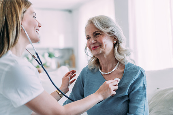 Paziente matura sorridente in ambiente domestico che si sottopone al controllo del cardiologo, regolarmente supportato dal suo ticket sanitario