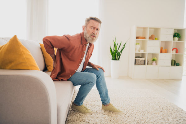 Uomo a casa che si appoggia sul divano dopo avere sperimentato senso di sbandamento e debolezza alle gambe