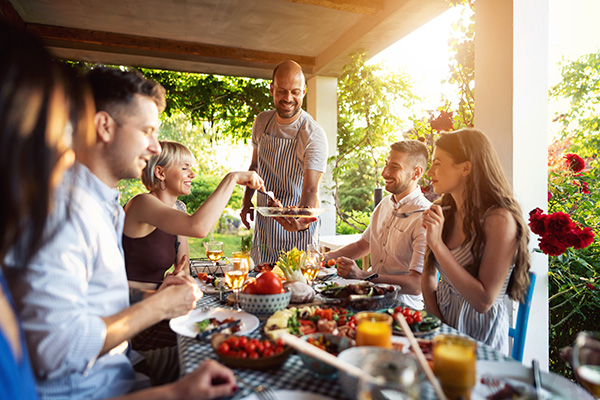 Uomo che serve agli amici delle pietanze fresche durante una cena estiva nel giardino di casa