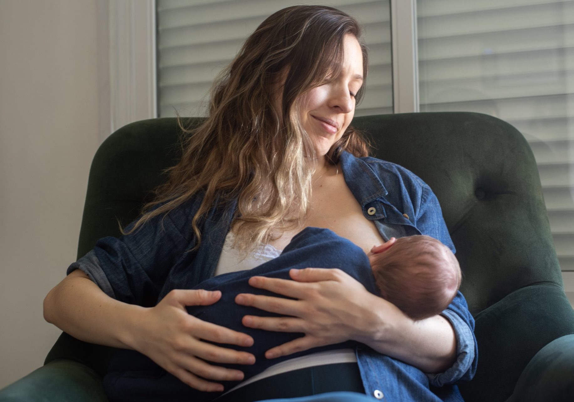 donna seduta in poltrona allatta al seno neonato
