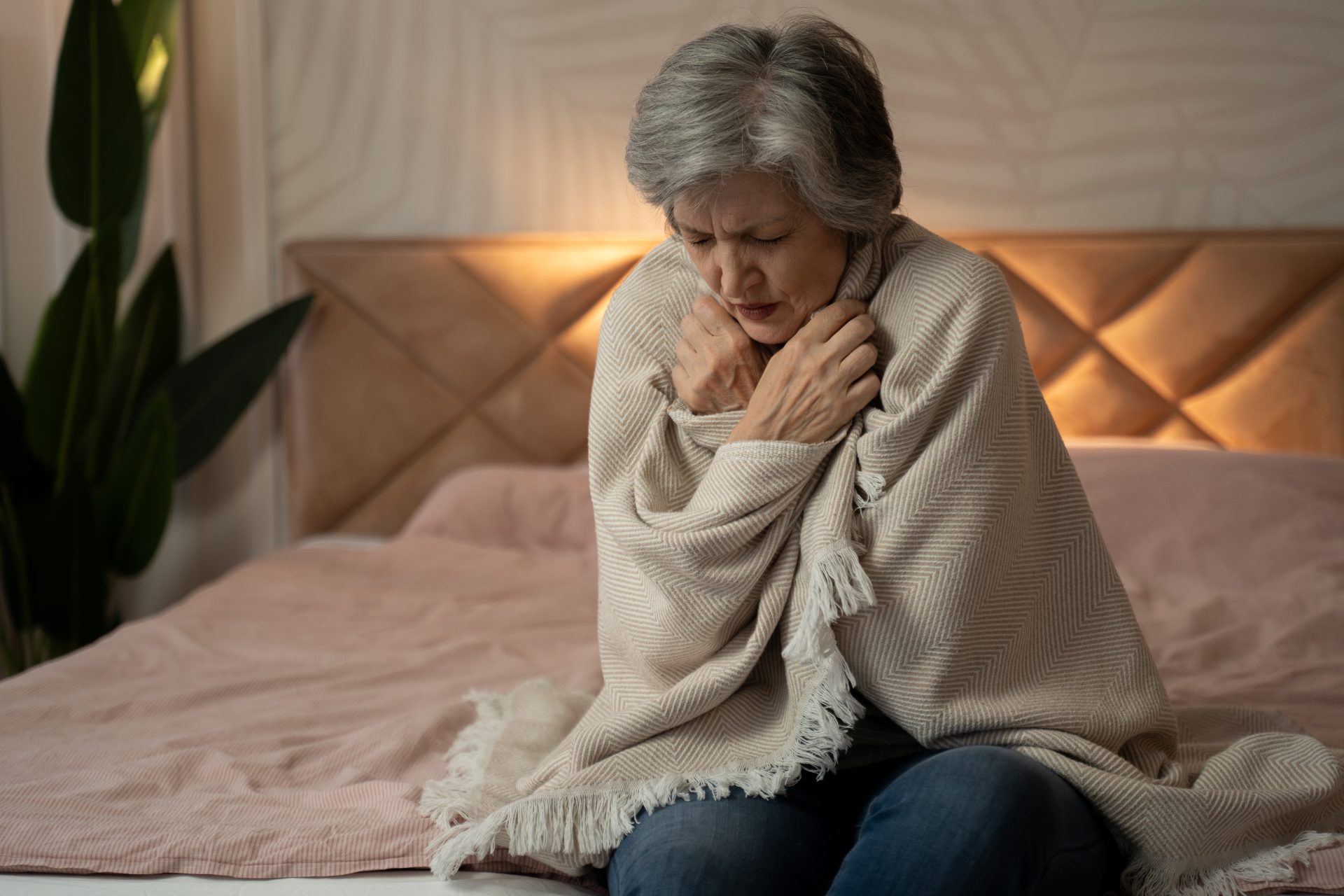 donna anziana seduta sul letto con coperta sulle spalle