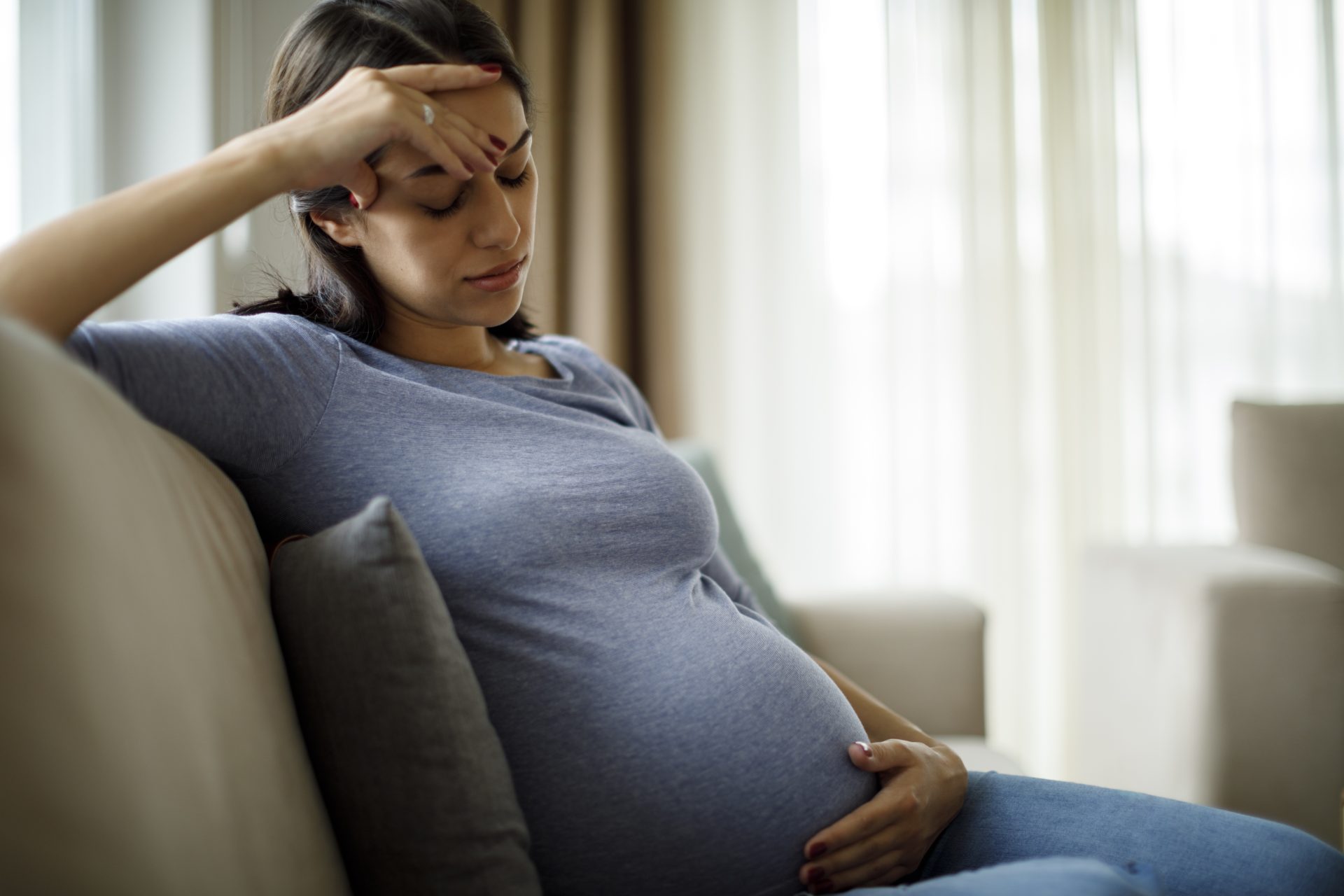 donna incinta stanca seduta sul divano che tocca la pancia