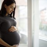 donna incinta tiene la pancia davanti alla finestra