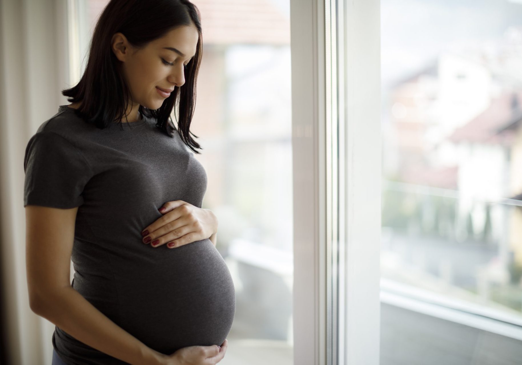 donna incinta tiene la pancia davanti alla finestra