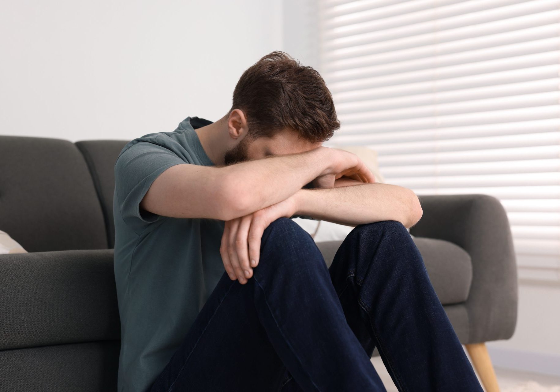 uomo depresso seduto a terra con testa sulle braccia