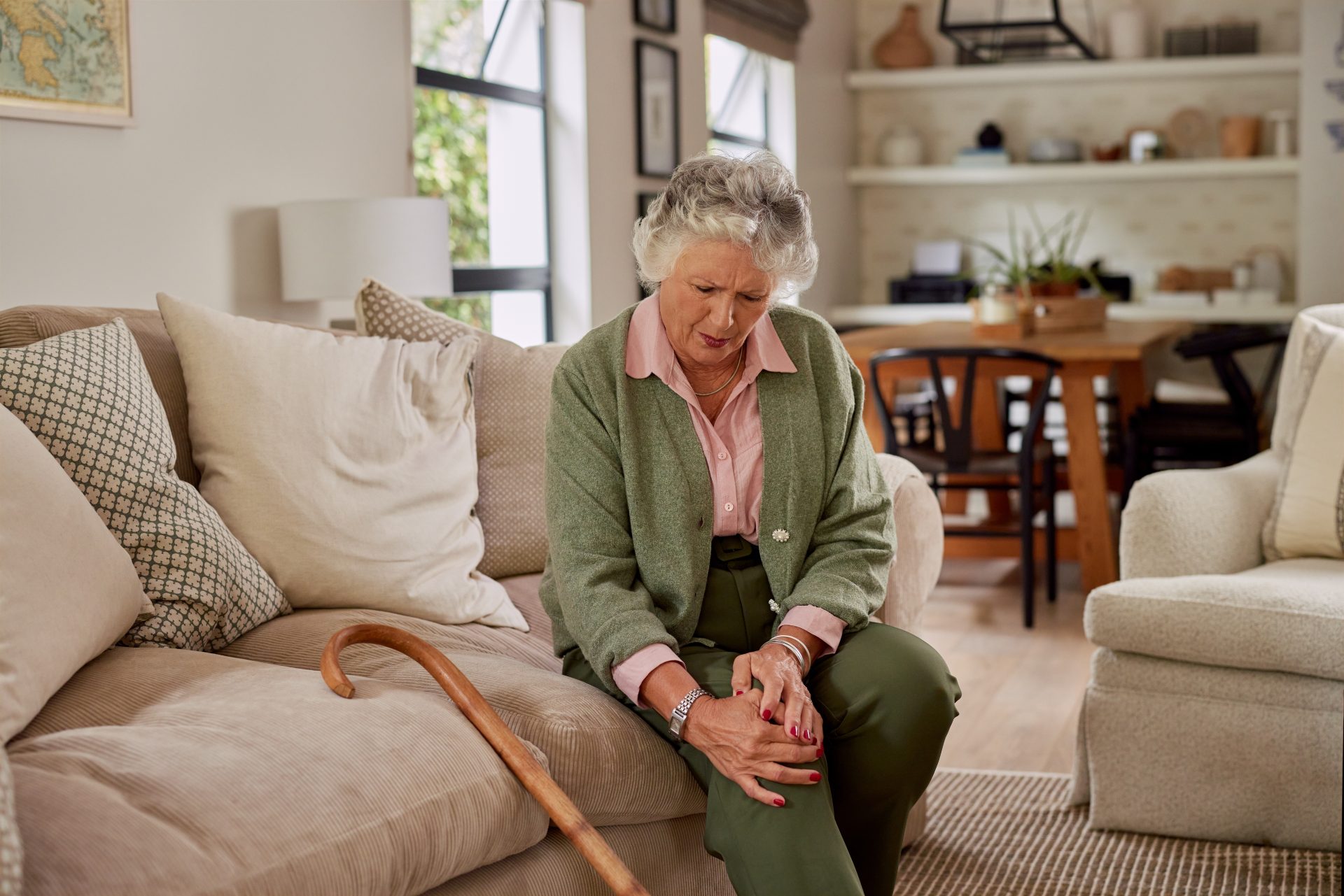 donna anziana seduta sul divano con dolore al ginocchio