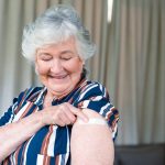 donna anziana guarda braccio con cerotto dopo vaccinazione