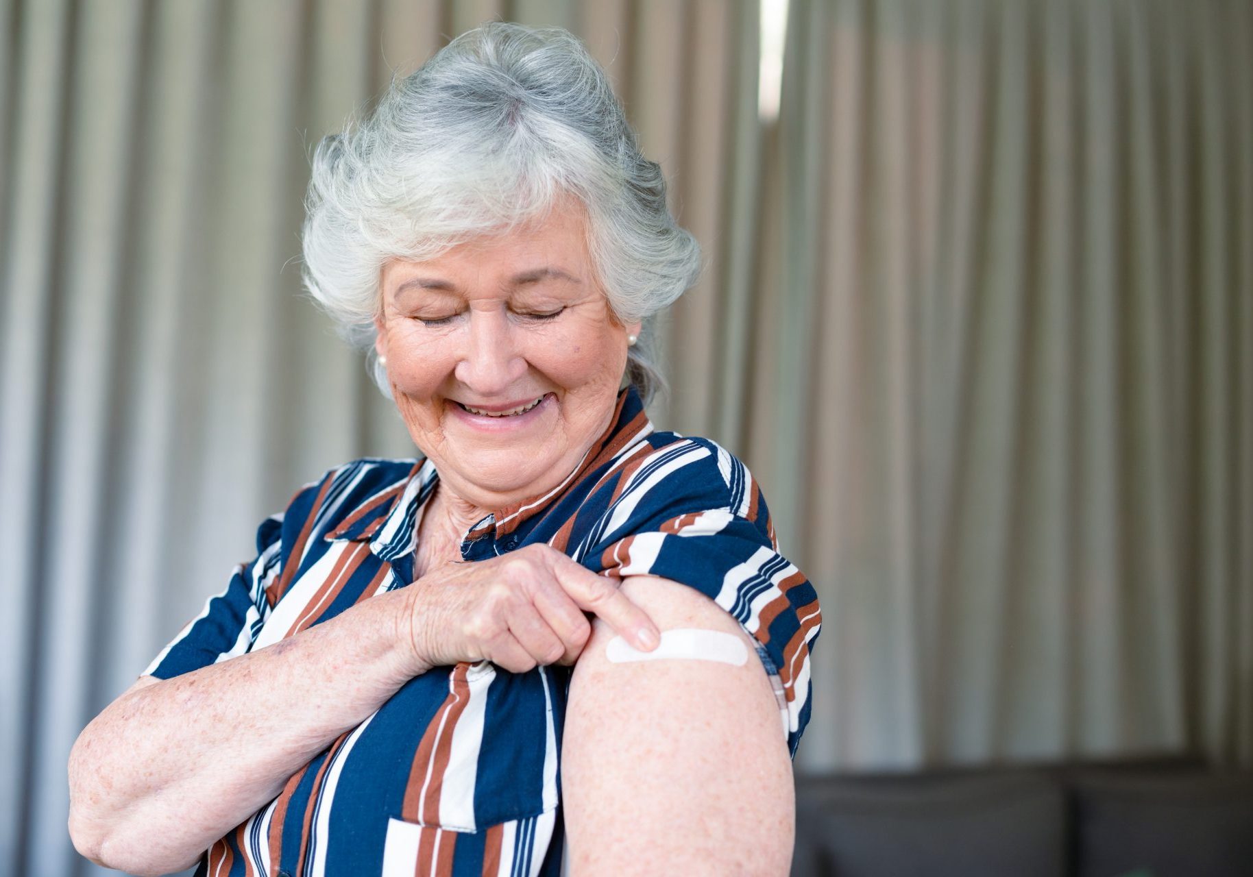 donna anziana guarda braccio con cerotto dopo vaccinazione