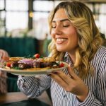 giovane donna sorridente tiene piatto con bistecca