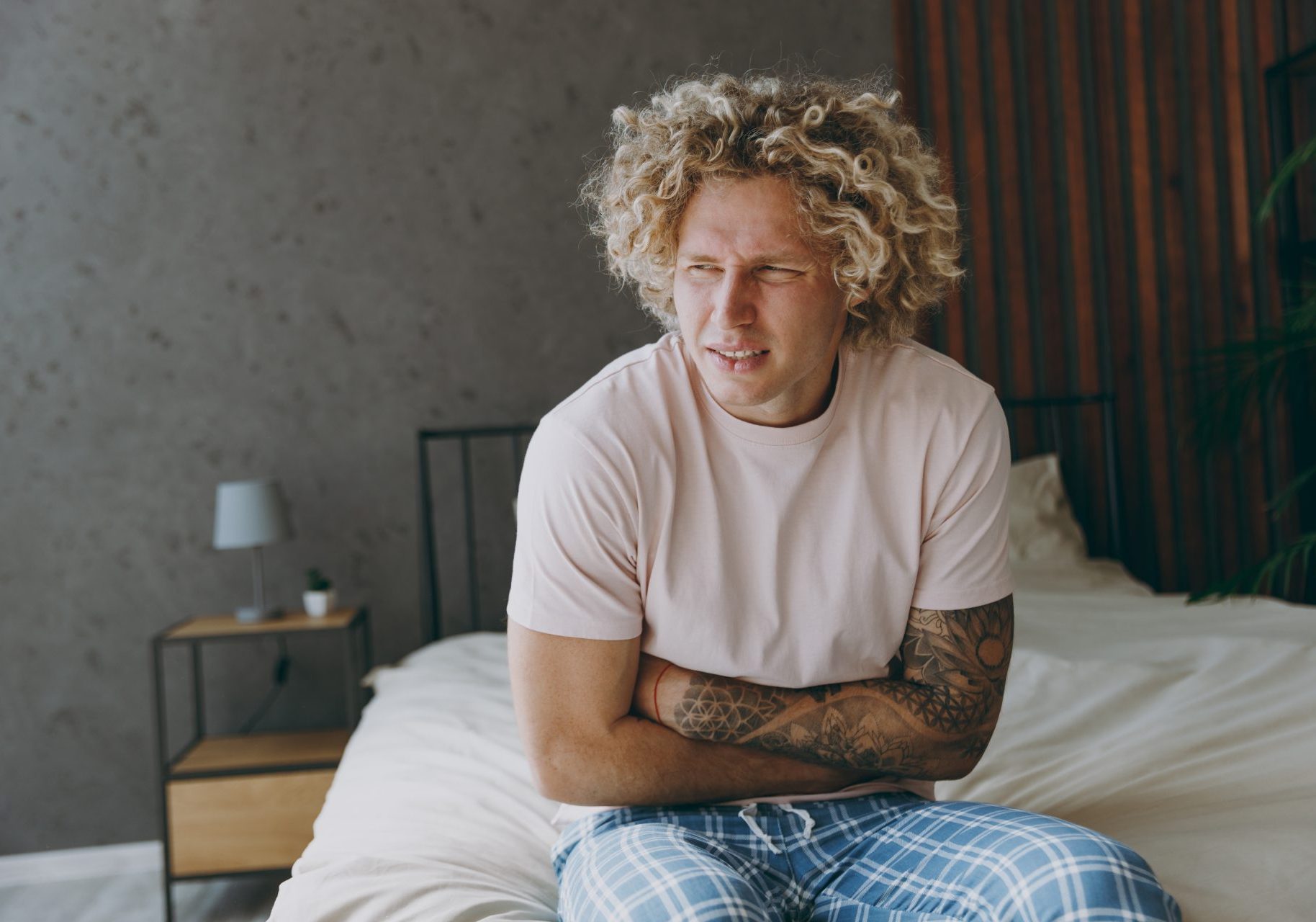 giovane uomo seduto sul letto con mal di stomaco