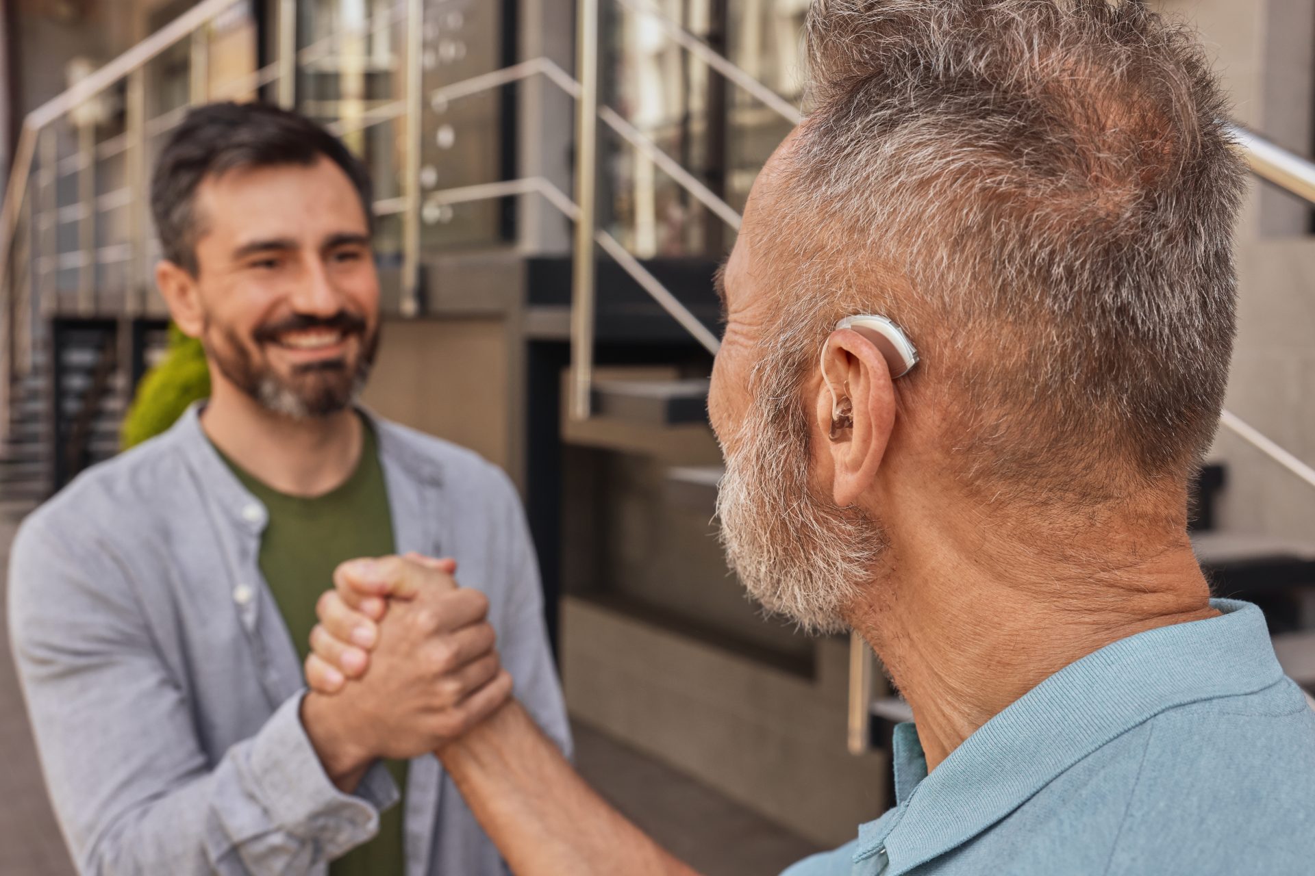 uomo con apparecchio acustico stringe la mano ad amico