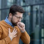 giovane uomo tossisce con mano al petto