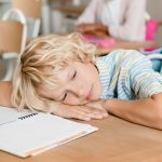 bambino stanco con testa poggiata sul banco di scuola