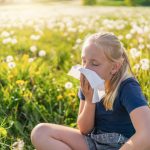 bambina in un prato soffia il naso per allergia alle graminacee
