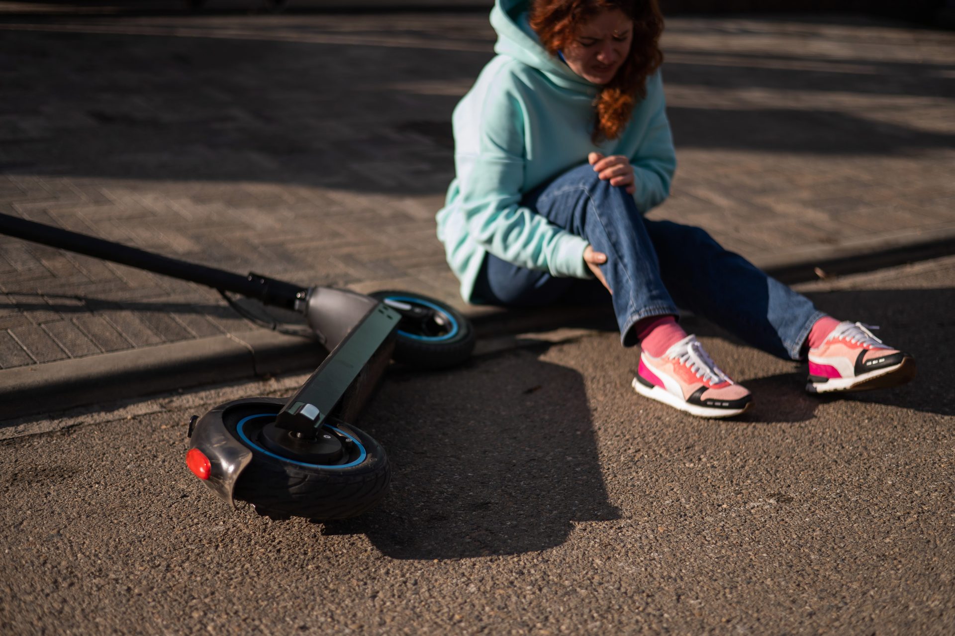 giovane donna seduta a terra dopo caduta dal monopattino