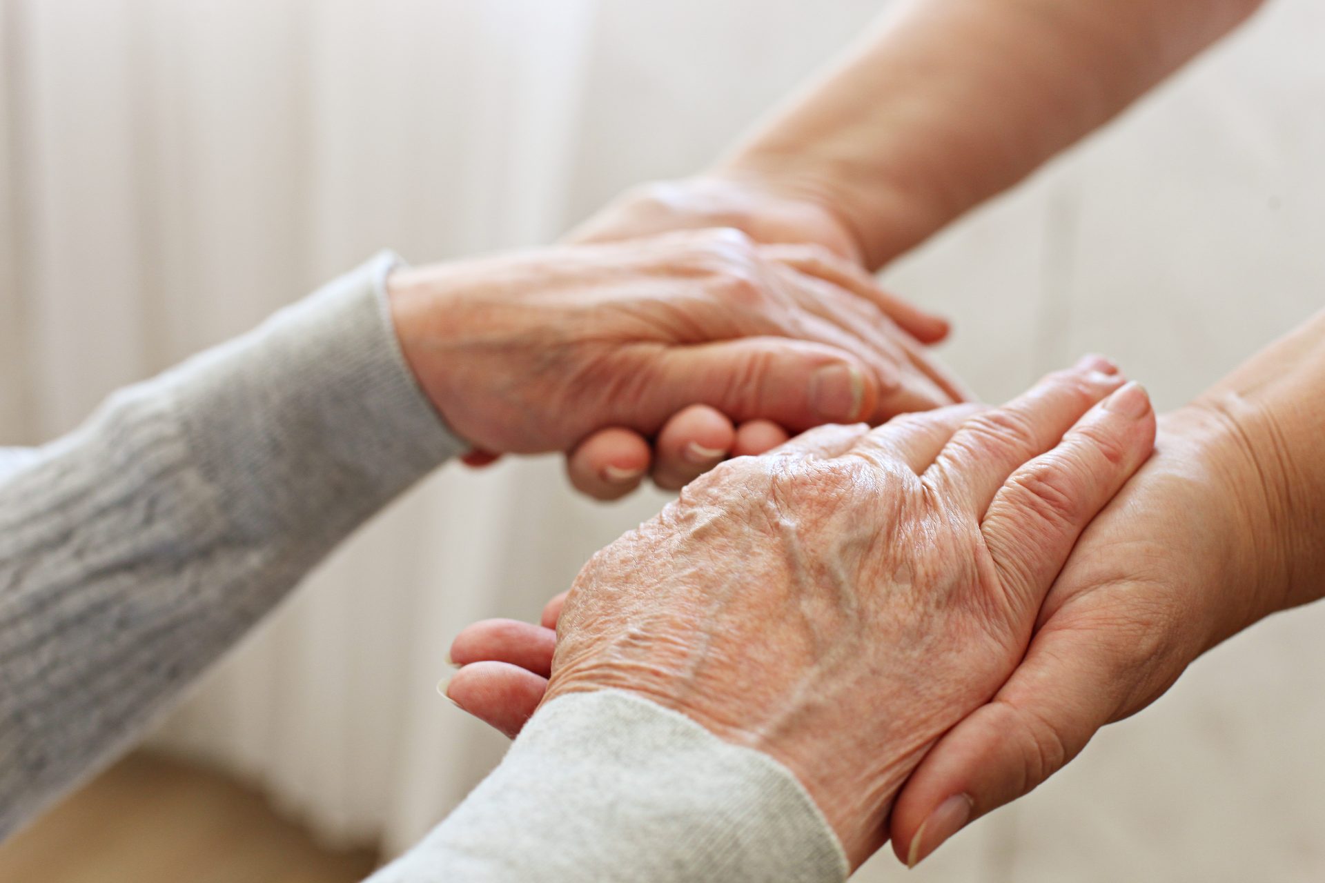 mani di caregiver stringono mani di persona anziana 