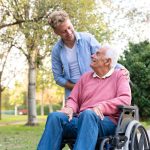 caregiver sorride a uomo anziano in sedia a rotelle