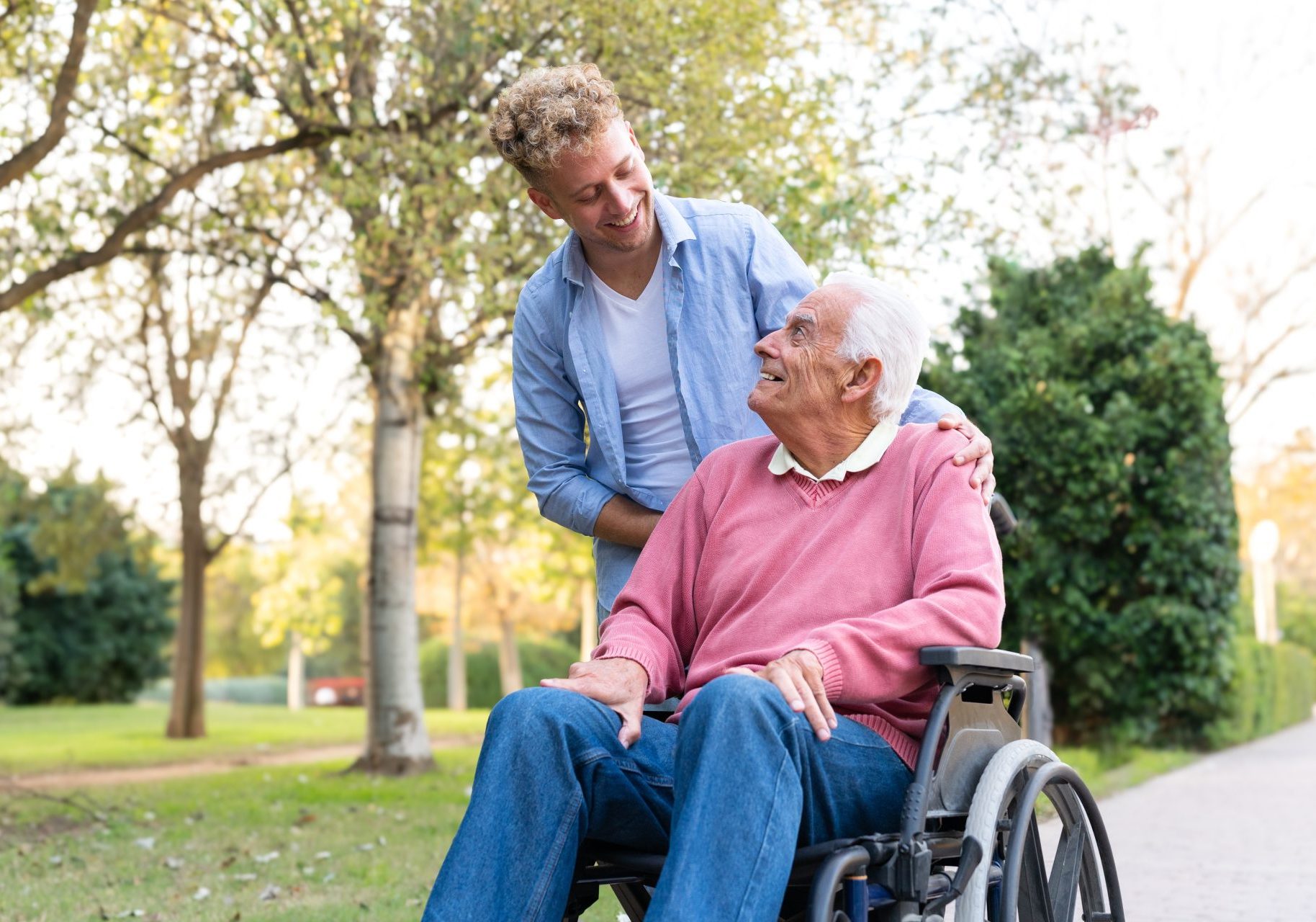 caregiver sorride a uomo anziano in sedia a rotelle