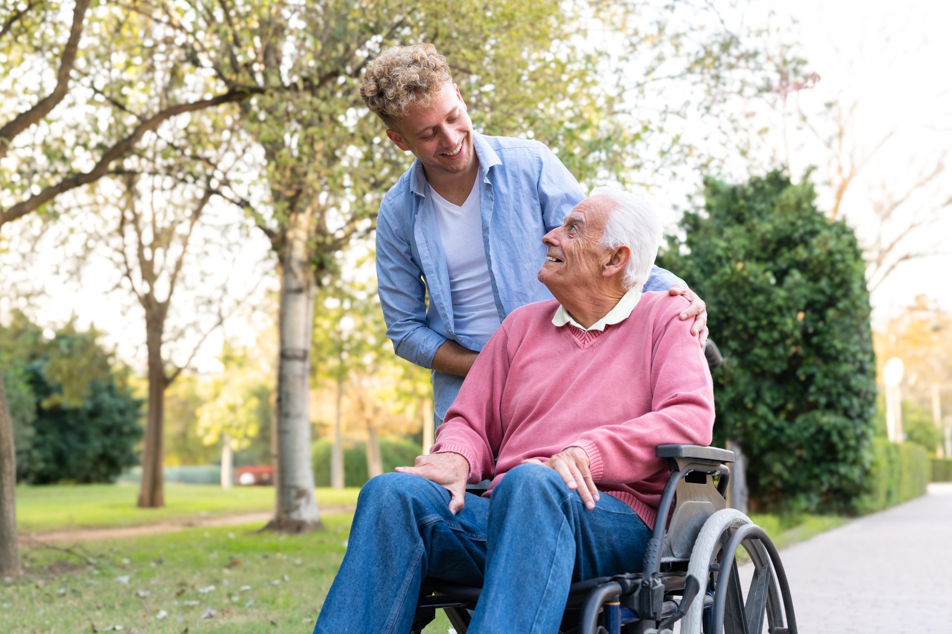 caregiver sorride a uomo anziano in sedia a rotelle