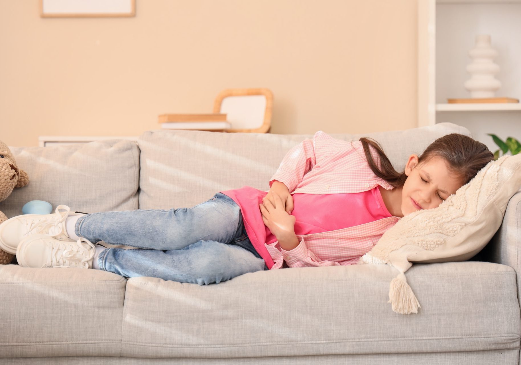 bambina distesa sul divano con mal di stomaco